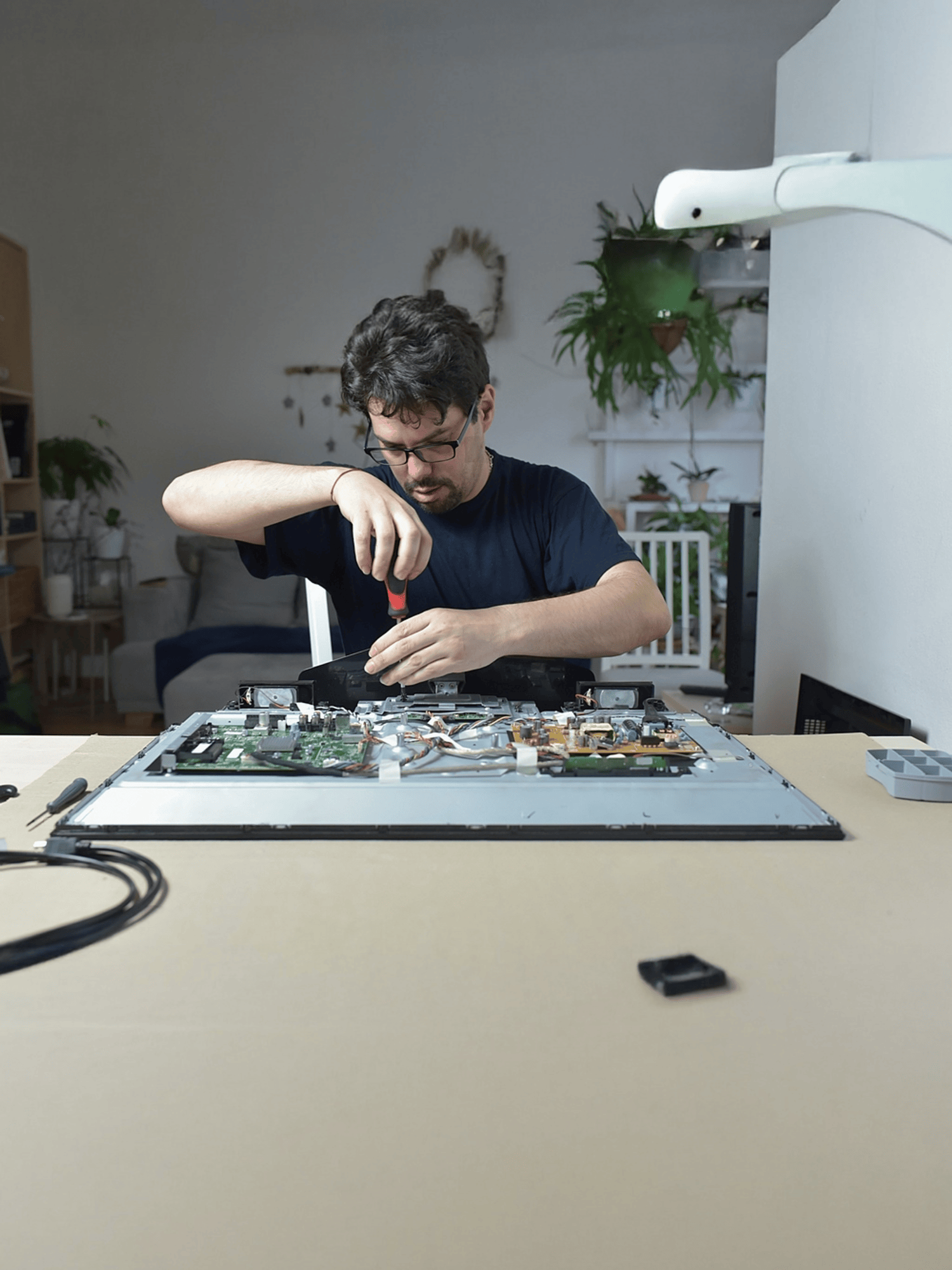 AK TV Repair Service Center technician carefully repairing the display panel of a flat-screen TV on a workbench, ensuring precise and expert service.