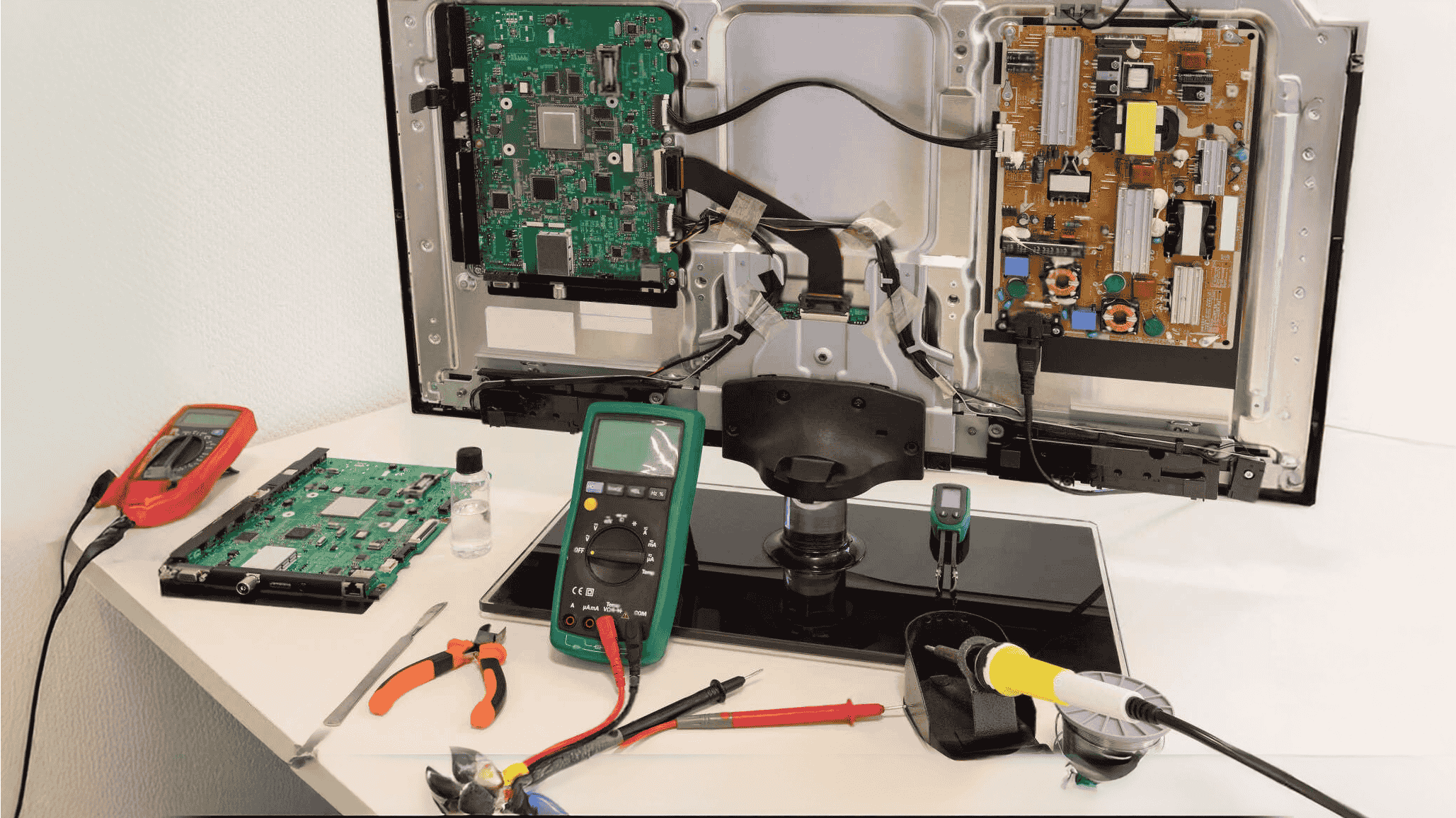 Smart TV motherboard and display panel undergoing professional diagnostics and repair at AK TV Repair Service Center, using precision tools and meters.