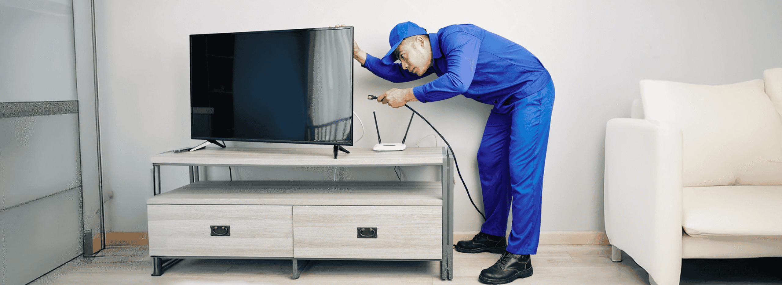AK TV Repair Service Center expert repairing a flat-screen TV—technician in blue uniform working with tools to fix connections in a modern living room.