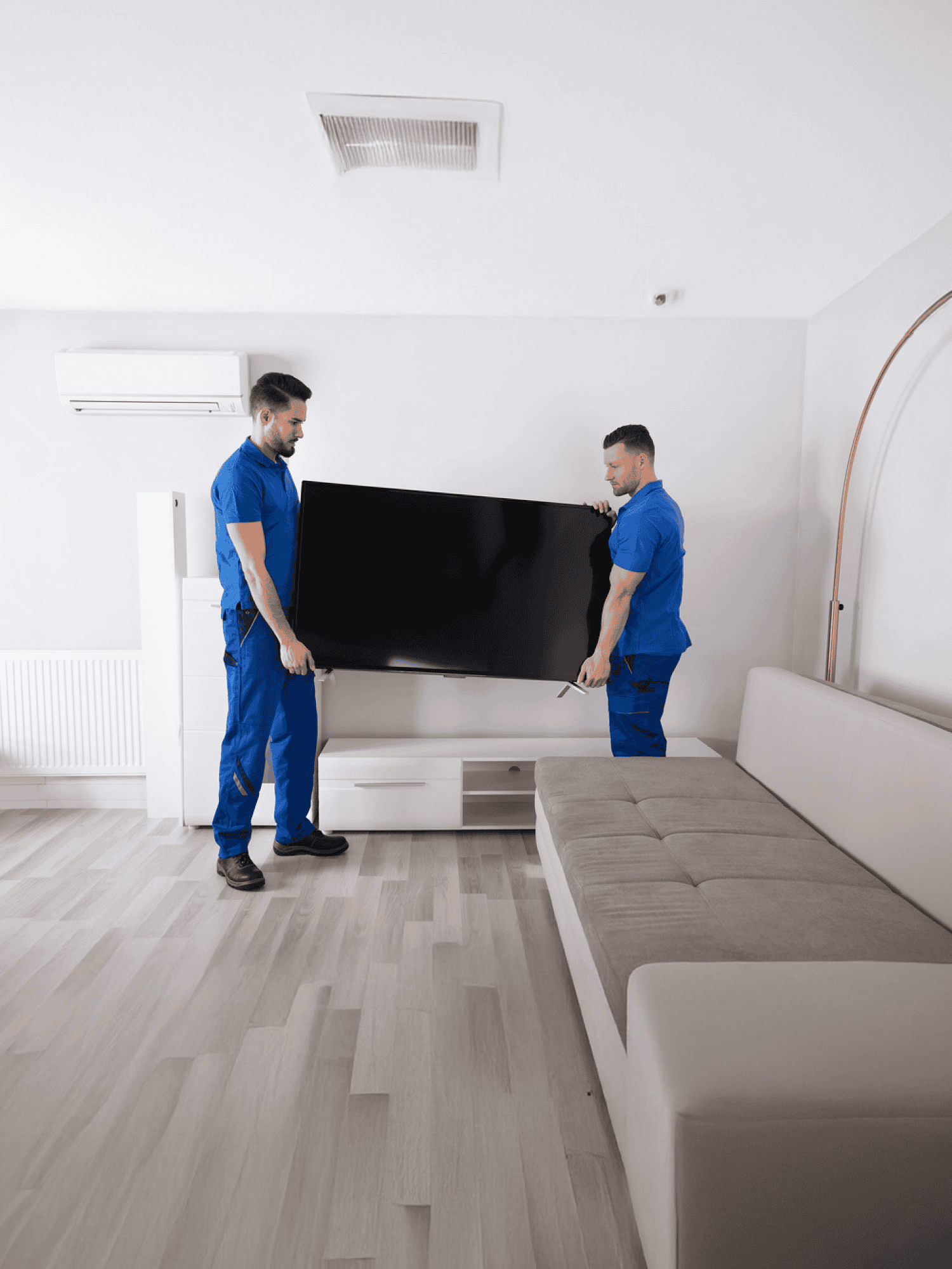 AK TV Repair Service Center experts pick up your TV for repairing—two uniformed technicians carefully handling a flat-screen TV in a modern living room setup.